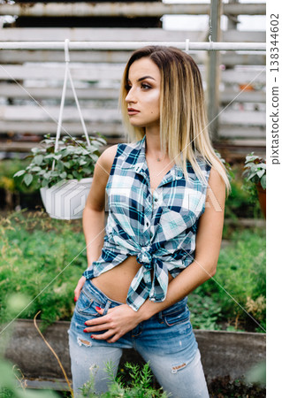 girl in long cardigan in plant shop chooses between two pots of pink flowers. Portrait of joyful lady in botanical garden. girl in long cardigan in plant shop chooses between two pots of pink flowers. Portrait of joyful lady in botanical garden. 138344602