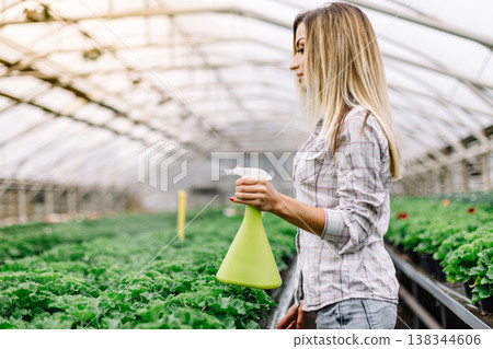 Portrait of smiling female florist watering plants in greenhouse. Portrait of smiling female florist watering plants in greenhouse. 138344606