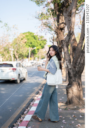 Full body asian woman holding coffee talking on phone while standing or waiting on sidewalk by road. Full body asian woman holding coffee talking on phone while standing or waiting on sidewalk by road. 138345207