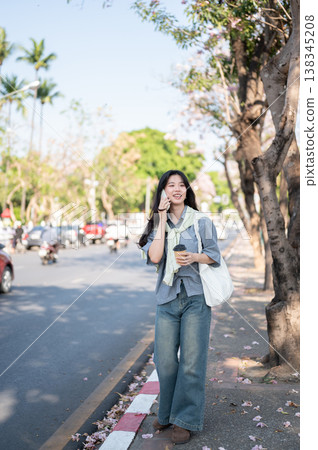 Full body asian woman holding coffee talking on phone as standing or waiting on sidewalk by the road 138345208