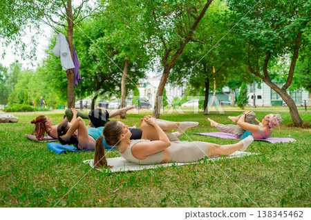 Ladies in athletic clothes exercising together raising knees to chest on mats in green park. Exercise, athletic, mats, park, group, raising knees, women. 138345462