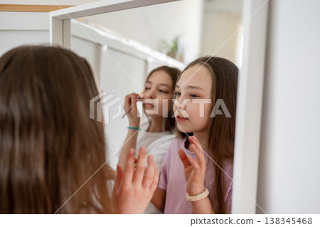 Two smiling girls applying makeup and laughing in home mirror with natural daylight. Makeup, mirror, laughing, girls, daylight, home, friendship. 138345468