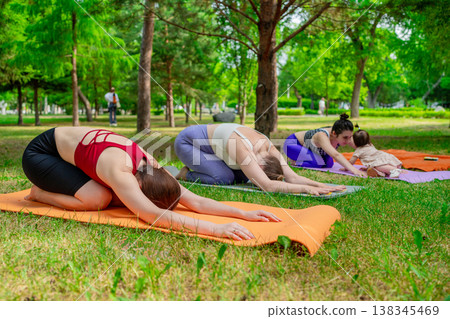 Group of women and kids relaxing in childs pose at end of yoga session on green grass. Childs pose, yoga, relaxing, group, session, grass. 138345469