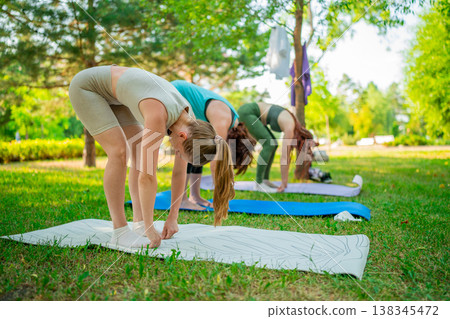 Two women stretching and bending forward during outdoor yoga session on mats in green park. Stretching, yoga, park, mats, women. 138345472