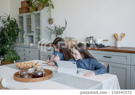 Two girls hugging and relaxing at kitchen table with plates of bread in sunlight home. Hugging, kitchen, bread, relaxing, girls, sunlight. Two girls hugging and relaxing at kitchen table with plates of bread in sunlight home. Hugging, kitchen, bread, relaxing, girls, sunlight. 138345572