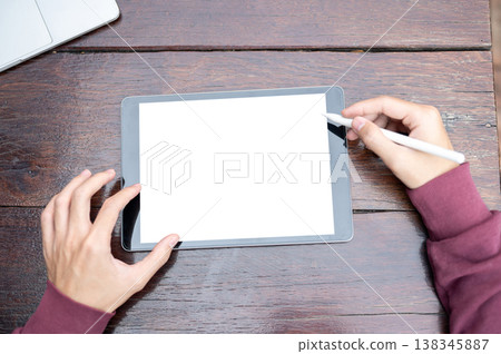 Top view of a man's hands holding stylus pen over white screen tablet while sitting at wooden table. 138345887