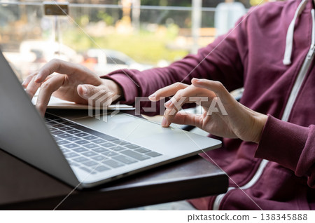 Close up of a young man's hands typing and looking at laptop while sitting at balcony table in cafe. 138345888