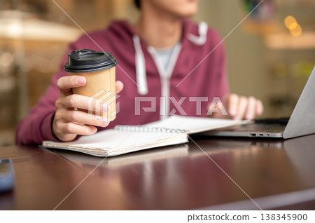 Close up of a man's hand holding coffee over notebook looking at laptop while sitting at cafe table. Close up of a man's hand holding coffee over notebook looking at laptop while sitting at cafe table. 138345900