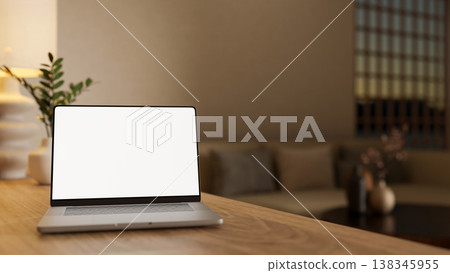 White screen laptop and potted plant on wooden counter table aside sofa couch in dim lit living room 138345955