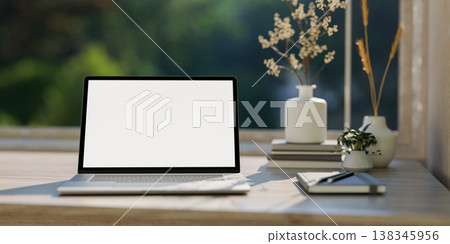 White screen laptop and books aside flower vase on wooden counter table by a window with garden view 138345956