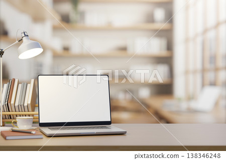 White screen laptop with coffee and book under lamp light on wooden table counter in cafe or library 138346248