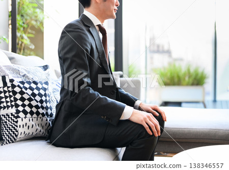 Side view of a man in a suit sitting on a sofa 138346557