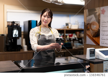 一位微笑的咖啡館員工隔著櫃檯遞給你一杯外帶咖啡。 一位微笑的咖啡館員工隔著櫃檯遞給你一杯外帶咖啡。 138346761