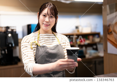 A smiling cafe employee hands over a takeaway coffee across the counter. A smiling cafe employee hands over a takeaway coffee across the counter. 138346763