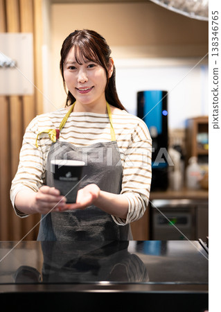 A smiling cafe employee hands over a takeaway coffee across the counter. 138346765
