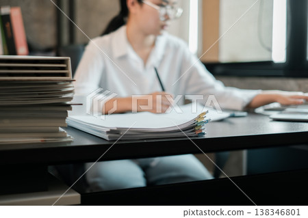 Professional woman in office setting working with documents and laptop, showcasing productivity and focus. 138346801