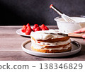 The process of decorating a homemade strawberry shortcake: The process of applying whipped cream. 138346829