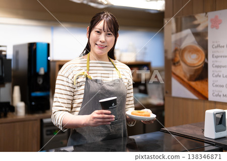 一位微笑的咖啡館員工正在販售咖啡和甜甜圈。 一位微笑的咖啡館員工正在販售咖啡和甜甜圈。 138346871