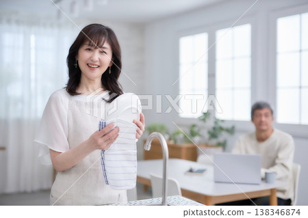 一對六十多歲的男女一邊在廚房擦碗碟，一邊微笑交談。 138346874