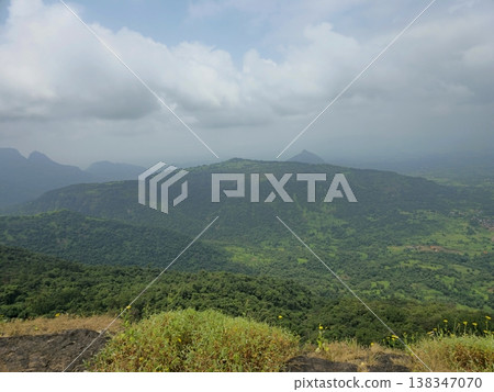 Wide view of lush green hills and valleys under cloudy skies, showcasing the scenic landscape and natural beauty of Matheran hill station. 138347070
