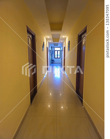 Long hotel corridor with polished floors, yellow walls, and evenly spaced doors, creating a clean, symmetrical perspective with depth and reflections. Long hotel corridor with polished floors, yellow walls, and evenly spaced doors, creating a clean, symmetrical perspective with depth and reflections. 138347095