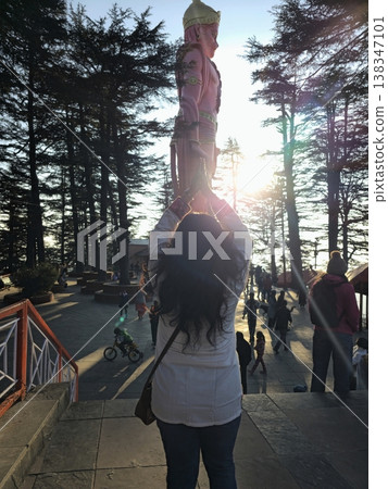 2nd Feb 2025,Shimla India Rear view of a visitor standing beneath the towering Hanuman statue at Jakhu Temple, framed by tall deodar trees and warm evening light. 2nd Feb 2025,Shimla India Rear view of a visitor standing beneath the towering Hanuman statue at Jakhu Temple, framed by tall deodar trees and warm evening light. 138347101