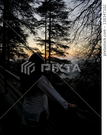 Silhouette of a woman standing near pine trees during sunset in Shimla, overlooking distant hills, creating a calm and reflective travel mood. Silhouette of a woman standing near pine trees during sunset in Shimla, overlooking distant hills, creating a calm and reflective travel mood. 138347102
