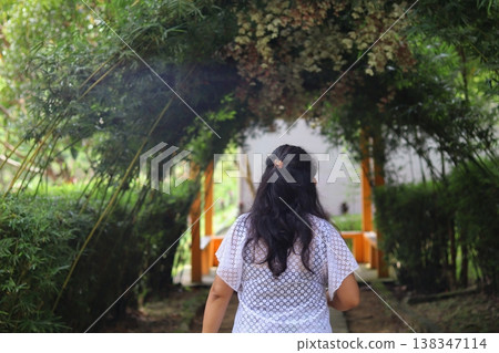 Woman walking through a green garden walkway in Kuala Lumpur, Malaysia, framed by plants and arches, expressing calm travel exploration. 138347114