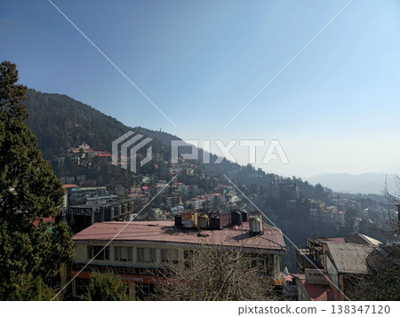 Urban hillside view of Shimla with layered buildings, pine-covered slopes, and clear blue sky, showing the dense mountain town layout and Himalayan terrain. Urban hillside view of Shimla with layered buildings, pine-covered slopes, and clear blue sky, showing the dense mountain town layout and Himalayan terrain. 138347120