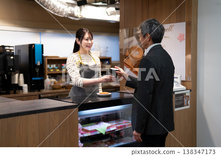 一位女咖啡店員工微笑地為顧客服務，並將顧客點的餐點遞給他們。 138347173