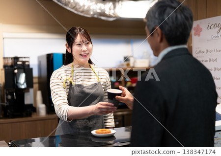 A female cafe employee smiles and serves customers, handing them their orders. A female cafe employee smiles and serves customers, handing them their orders. 138347174