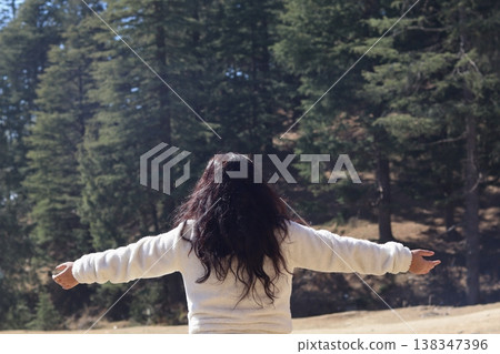 Woman standing with open arms facing tall pine trees in Shimla, expressing peace, adventure, and connection to nature. 138347396