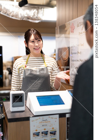 A smiling cafe employee guides customers to pay with electronic money at the register. 138348054