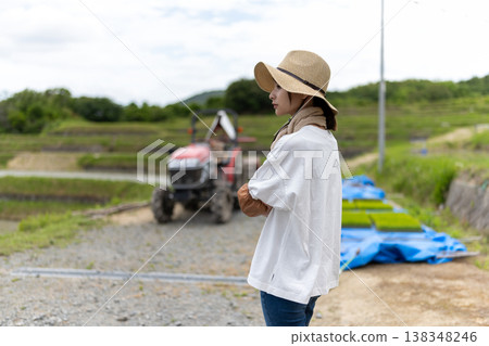 A female farmer gazes at her tractor and rice paddy. 138348246