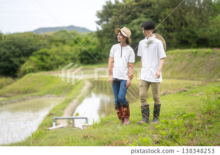 一對年輕的農夫夫婦走在稻田旁。 138348253