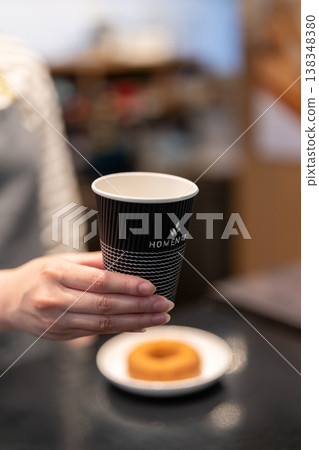 A female employee at a cafe hands over a coffee for takeout. A female employee at a cafe hands over a coffee for takeout. 138348380