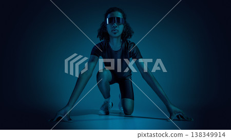 Female teenager athlete in running start pose in minimal dark studio with blue lighting. Female teenager athlete in running start pose in minimal dark studio with blue lighting. 138349914