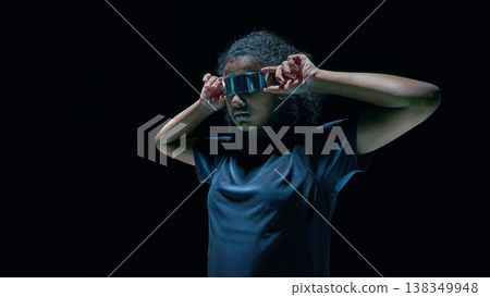 Teenager adjusting futuristic visor with augmented reality UI overlays in dark studio 138349948