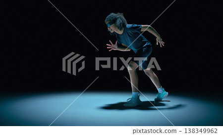 Teenager athlete running with futuristic visor and holographic UI overlays in dark studio. Teenager athlete running with futuristic visor and holographic UI overlays in dark studio. 138349962