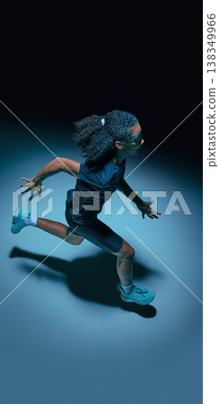 Female teenager athlete running forward wearing futuristic visor in dark minimal studio. 138349966