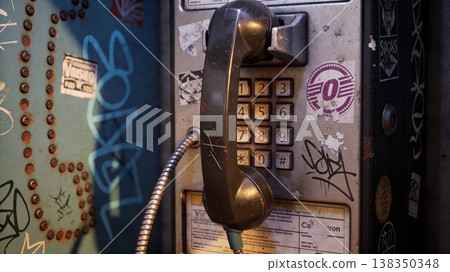 Weathered vintage public payphone covered in colorful graffiti and torn stickers on a city street, representing obsolete technology and urban decay 138350348