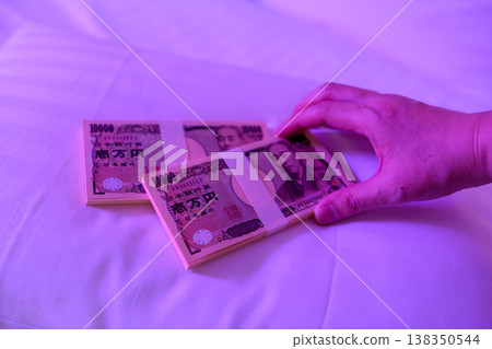 床上，一隻手緊緊握著一沓現金。 138350544
