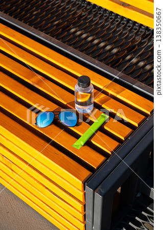 Water bottle with sunglasses and green powder sachet on yellow wooden bench. 138350667