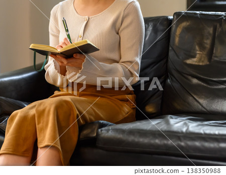 A woman writing in a notebook on a sofa. 138350988
