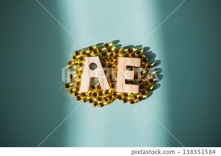 letters A and E sit on cluster of yellow translucent softgel capsules on teal background. Vitamin A and E combination, free radical defense, antioxidant complex, cellular longevity. letters A and E sit on cluster of yellow translucent softgel capsules on teal background. Vitamin A and E combination, free radical defense, antioxidant complex, cellular longevity. 138351584
