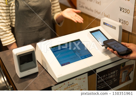 A hand using a smartphone to make a cashless payment at the cafe's register. A hand using a smartphone to make a cashless payment at the cafe's register. 138351961