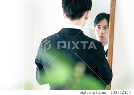 A man in a suit adjusts his appearance in front of a mirror. A man in a suit adjusts his appearance in front of a mirror. 138352593