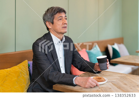 一位資深商人面帶微笑,在咖啡館休息時享用咖啡和甜甜圈。 一位資深商人面帶微笑,在咖啡館休息時享用咖啡和甜甜圈。 138352633