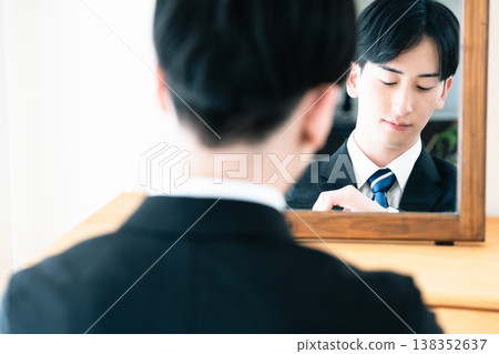 A man in a suit adjusts his appearance in front of a mirror. 138352637