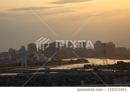 A view of the sunset sky, the cityscape of buildings, a river, and a bridge. A view of the sunset sky, the cityscape of buildings, a river, and a bridge. 138352841